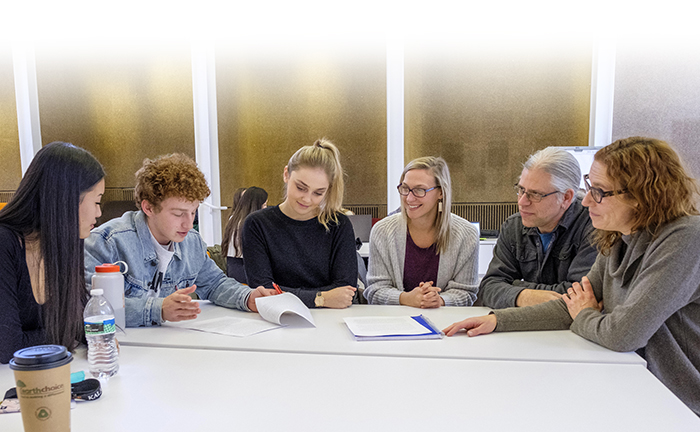 Professor Amelia Katanski sitting at a table with a group of students looking at papers