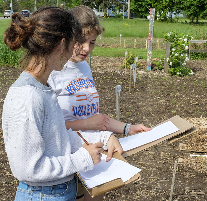 Two students drawing layouts of the garden they are standing at