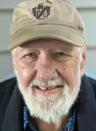 Hugh Frederick Mehaffie Jr. '57, an older man with a white beard, smiling while wearing a beige baseball cap with a 'PC' logo and a dark jacket over a blue collared shirt, against a light outdoor background.