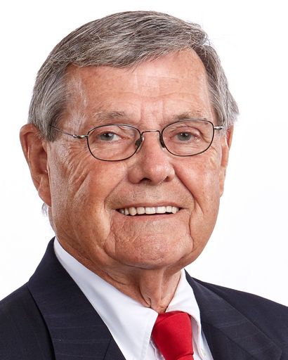 Ronald Nelson Kilgore '58, an older man with gray hair and glasses, smiling while wearing a dark suit, white dress shirt, and red tie, against a plain white background."