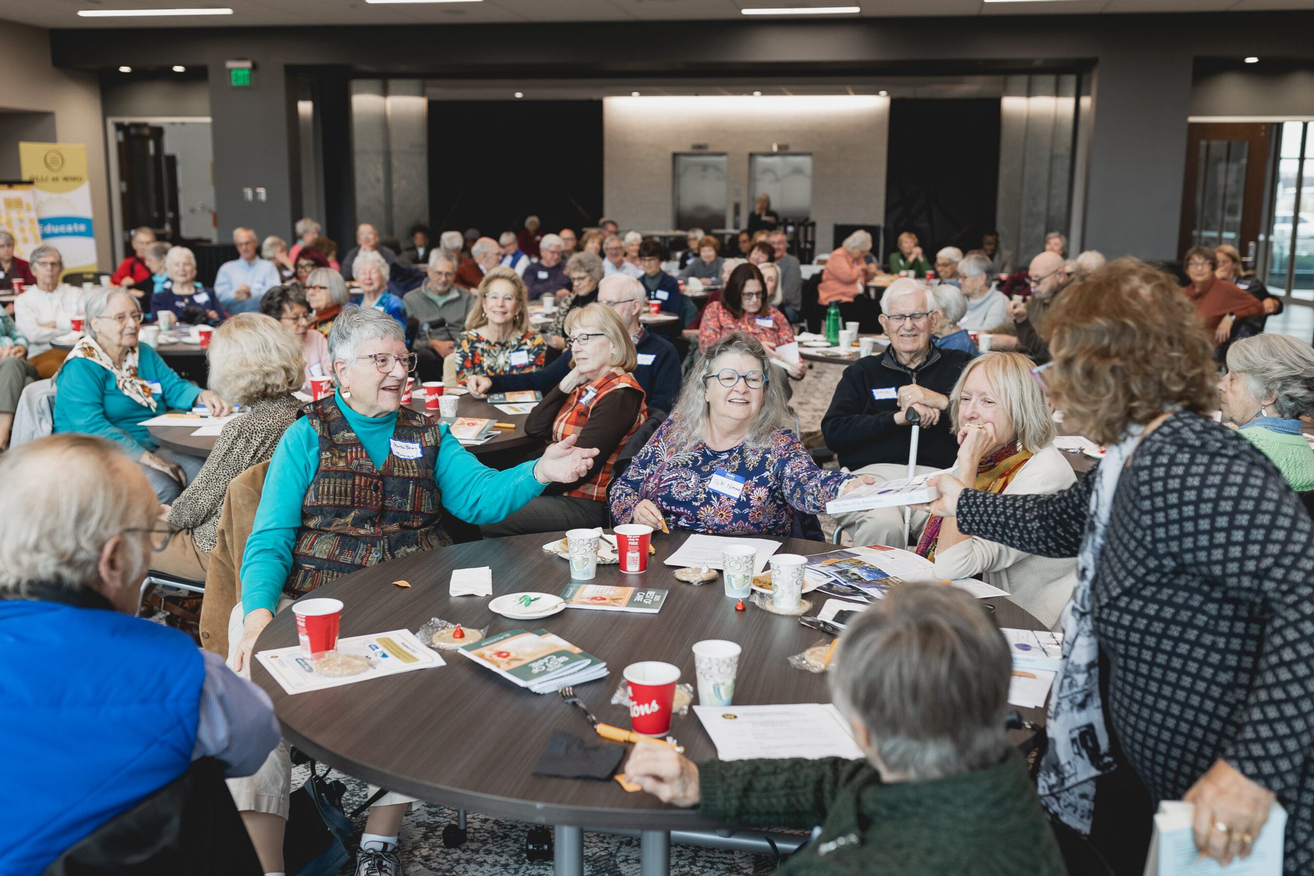 A lively group of mature adults engaged in a discussion at a round table during an Osher Lifelong Learning Institute (OLLI) event, part of Kalamazoo College’s new partnership with Western Michigan University.