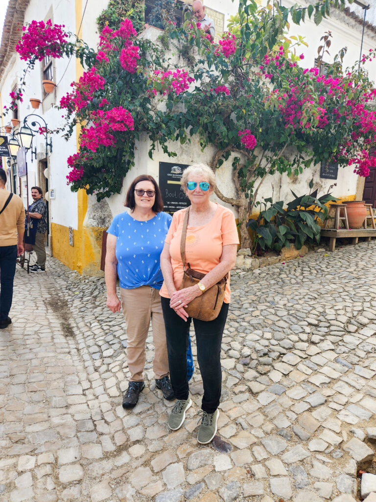 Photo of Deb Russell ’76 and Barb Slinker ’76 standing together on a cobblestone street during a trip to a scenic European-style village.